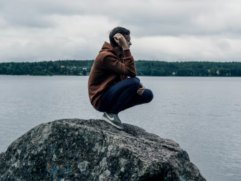 man crouching on rock looking at sea