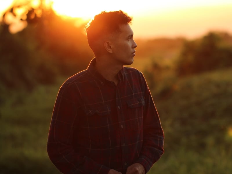 man in black and white plaid dress shirt standing on green grass during sunset