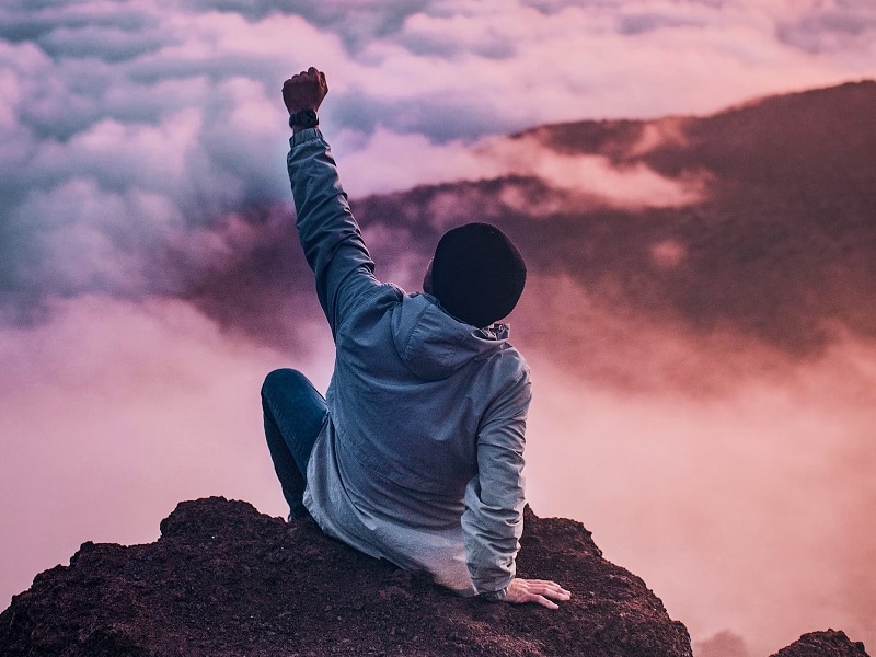 person on mountain overlooking clouds