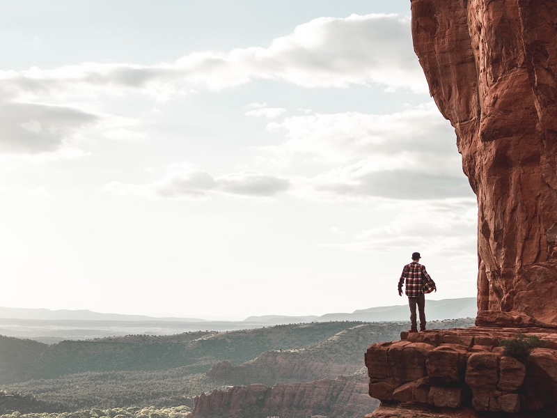 person standing on cliff looking out over valley